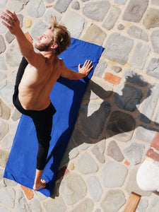 A man in a yoga pose on his sapphire blue yoga mat towel outside.
