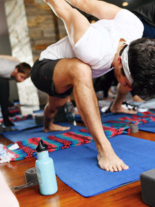 A man in a yoga pose standing on a sapphire blue yoga mat towel.