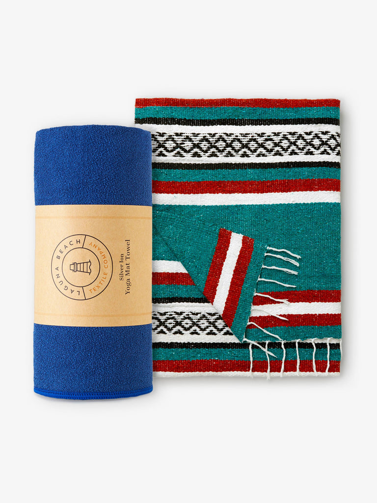A rolled up sapphire blue yoga mat towel next to a green and red striped Mexican blanket.
