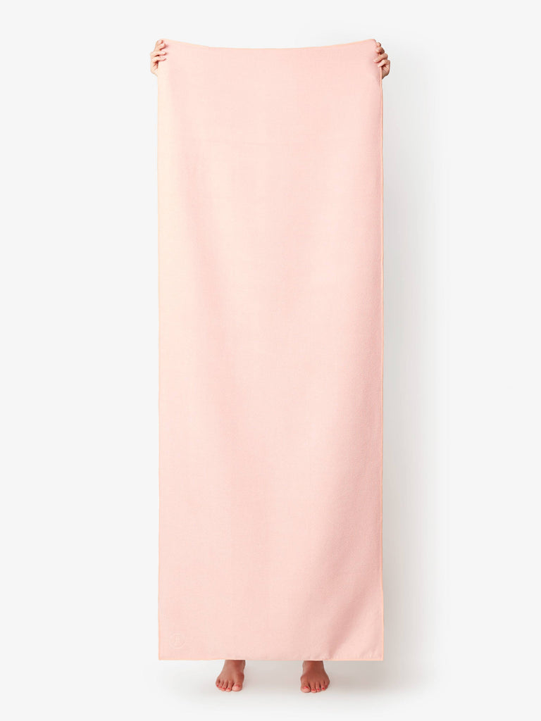 A blush colored yoga mat towel being held up by a person.