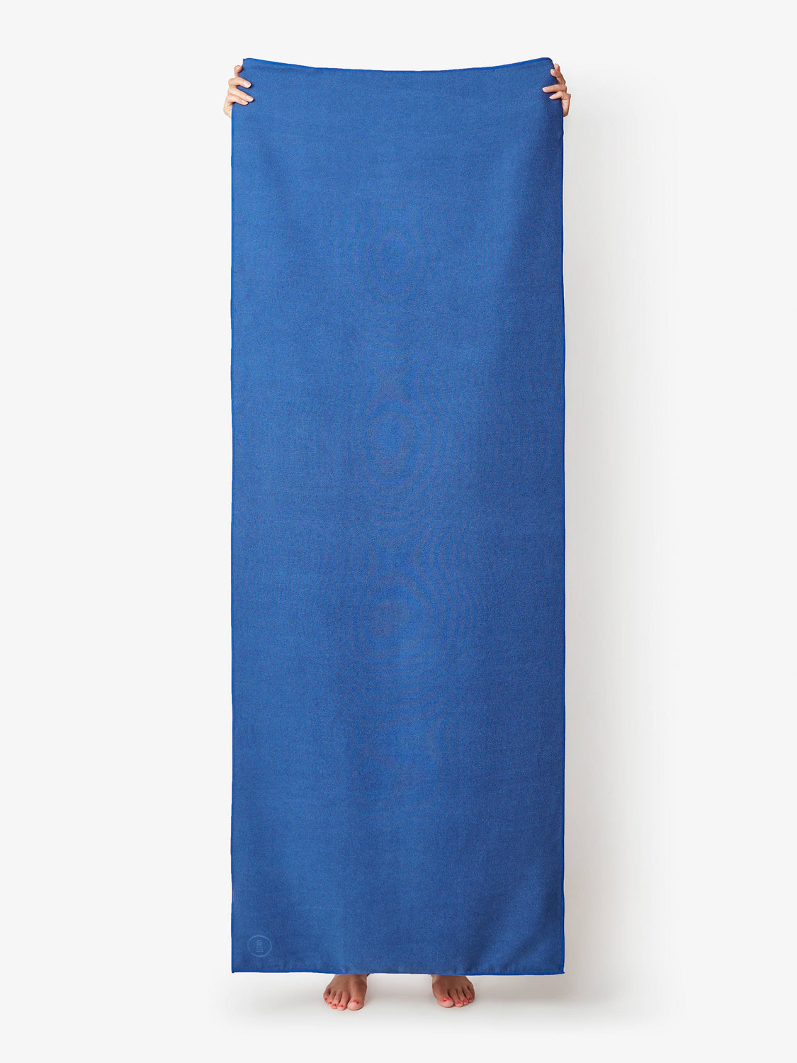 A sapphire blue yoga mat towel being held up by a person.